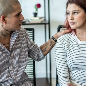 Man legt troostend hand op schouder jonge vrouw