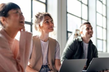 Jonge vrouw achter latop lacht en lijkt naar collega