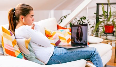 Jonge vrouw zit met laptop op schoot in een online gesprek