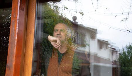 Man kijkt hoopvol uit het raam van zijn huis