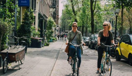 Twee vrouwen fietsen op de bakfiets over de grachten van Amsterdam
